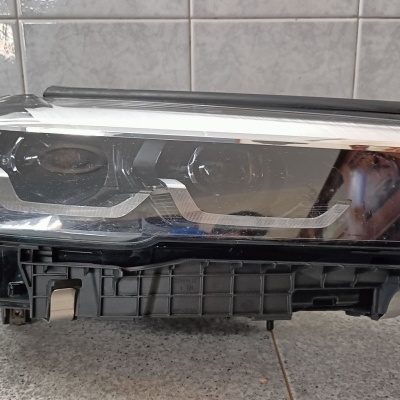 Farol dianteiro de automóvel preto com lente de vidro transparente sobre superfície de azulejos cinzentos.