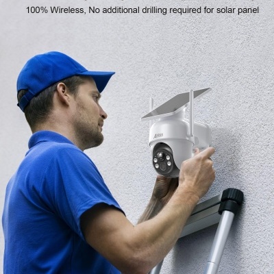 Homem a instalar câmara de segurança branca com painel solar numa parede cinzenta