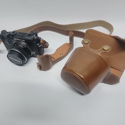 Câmara Olympus PEN-F preta com lente e estojo de couro castanho claro.