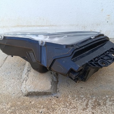 Farol dianteiro para automóvel preto com lente transparente sobre chão de cimento