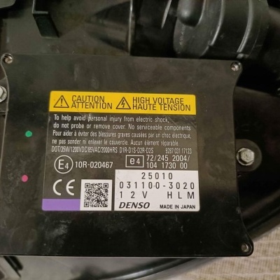 Componente automóvel Denso preto com etiqueta técnica e aviso de alta tensão