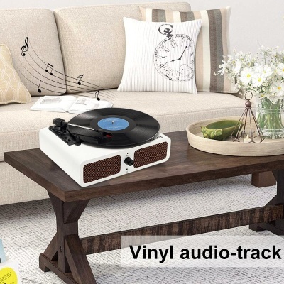 Toca-discos branco com vinil preto numa mesa de madeira escura à frente de sofá bege com almofadas e flores