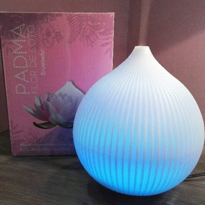 Difusor branco iluminado em azul com embalagem rosa ao lado