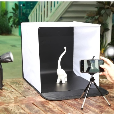 Cubo de luz branco com interior preto para fotografia, figura branca de gato, smartphone em tripé e luzes externas