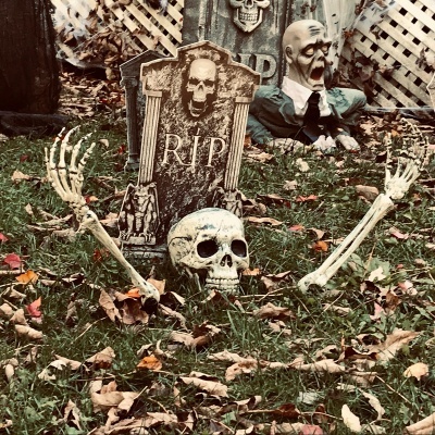 Decoração macabra de Halloween com crânio, mãos esqueléticas, caixão RIP e zumbi numa relva com folhas secas