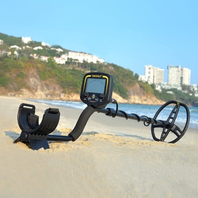 Detector de metais preto e amarelo na areia da praia com mar e edifícios ao fundo