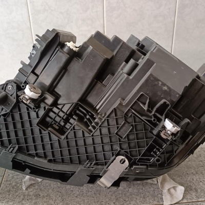 Peça automóvel preta em plástico com várias formas, sobre chão de azulejos cinzentos