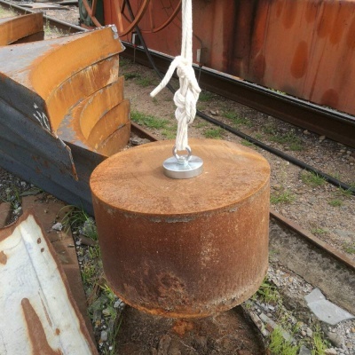 Cilindro metálico enferrujado suspenso por corda branca ao ar livre