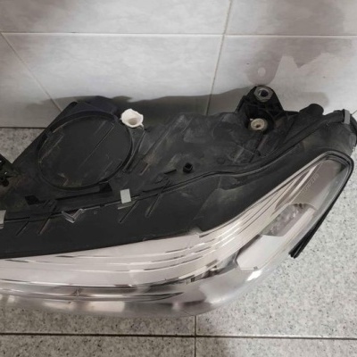 Farol automóvel preto com lente transparente sobre chão de azulejos cinzentos