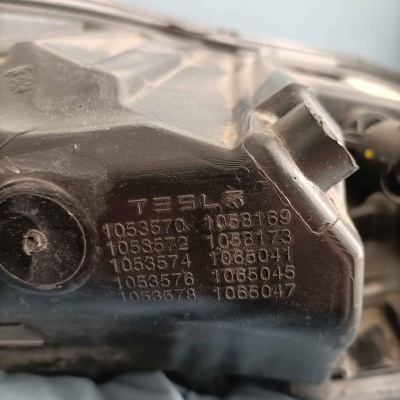 Componente automóvel preto de plástico com o texto TESLA e números gravados em relevo