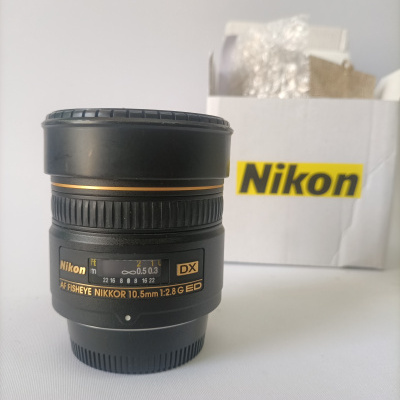 Objetiva fotográfica preta Nikon com caixa branca ao fundo