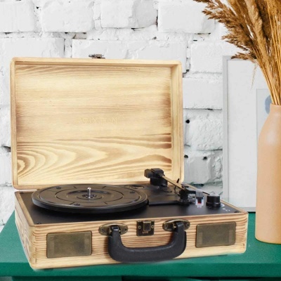 Máquina de vinil portátil em madeira clara com tampa aberta sobre superfície verde