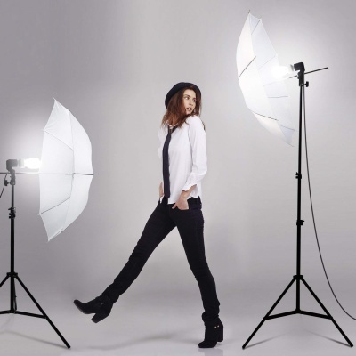 Mulher com roupa preta e branca num estúdio de fotografia entre luzes com guarda-chuvas brancos