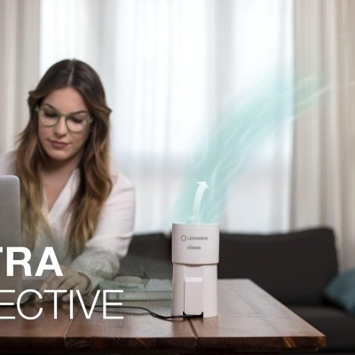 Humidificador branco em mesa junto a mulher a trabalhar no portátil