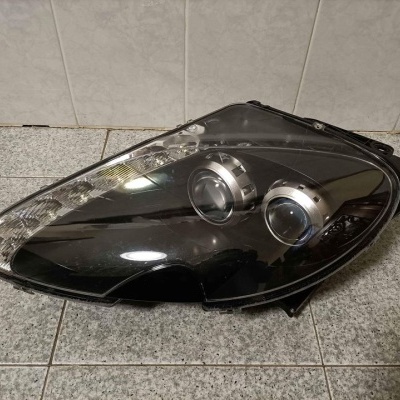 Farol dianteiro automóvel preto com lentes transparentes em superfície de azulejos