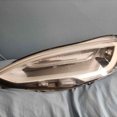 Farol dianteiro de automóvel com estrutura preta e lente transparente sobre tecido azul claro