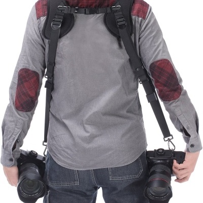 Pessoa de costas com arnês preto segurando duas câmaras fotográficas
