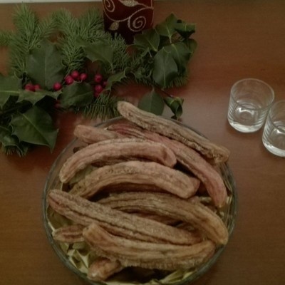 Prato de vidro com carne seca numa mesa com decoração verde e dois copos ao lado.
