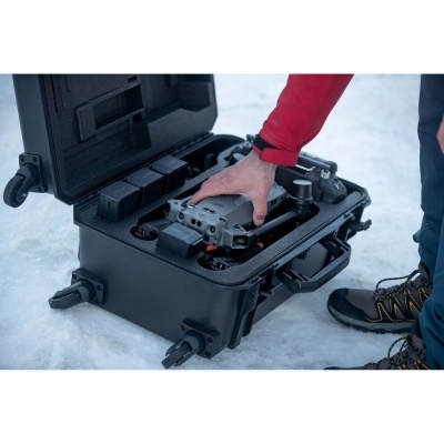 Mala de transporte preta aberta com drone cinzento e acessórios no gelo, pessoa a segurar o drone