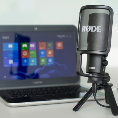 Microfone RØDE preto com suporte tripé e portátil Toshiba com ecrã do Windows em fundo branco