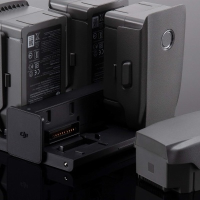 Baterias cinzentas DJI para drone em suporte de carregamento sobre superfície preta reflexiva