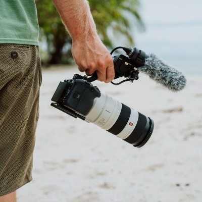 Homem segurando câmara fotográfica com lente longa e microfone na praia
