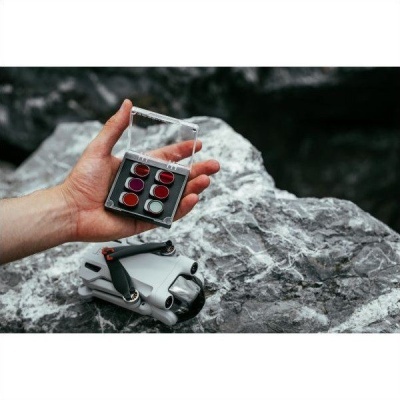 Mão segura caixa transparente com batons vermelhos e roxos sobre pedra com estojo cinzento ao lado