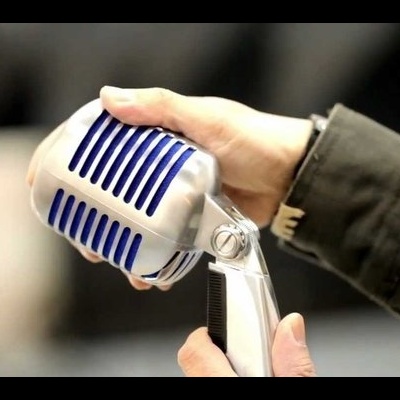 Microfone retro prateado com detalhes em azul segurado por uma mão