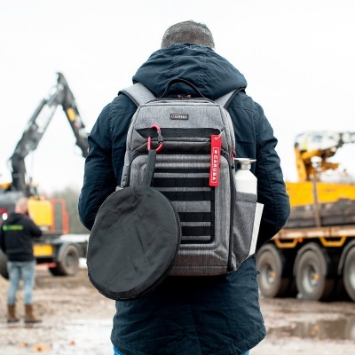 Mochila cinzenta com suporte para garrafa e bolsa preta pendurada, usada em ambiente de construção