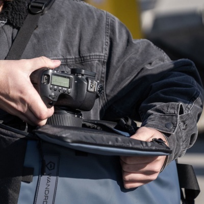 Câmera DSLR preta na mão sobre bolsa cinza aberta