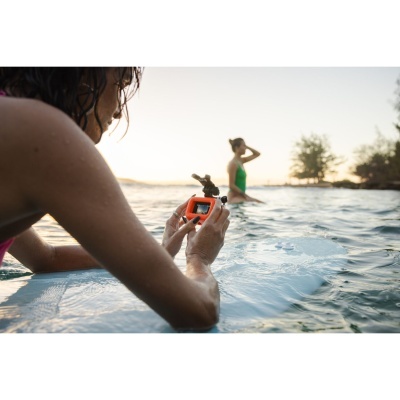 Pessoa na água a segurar uma câmara de ação laranja com outra pessoa ao fundo