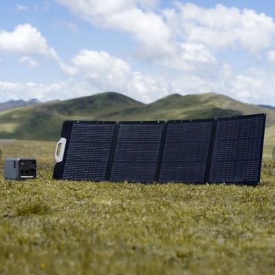 Painel solar portátil com quatro placas pretas ligado a caixa elétrica cinzenta em campo verde