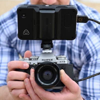 Câmara Fujifilm X-T3 com lente e monitor externo a ser segurada por pessoa.
