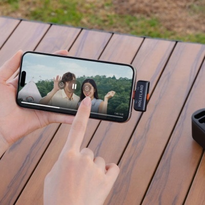 Smartphone a exibir fotografia, caixa de auscultadores pretos numa mesa de madeira ao ar livre