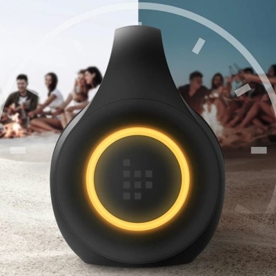 Coluna portátil preta com círculo luminoso amarelo numa praia com pessoas ao fundo