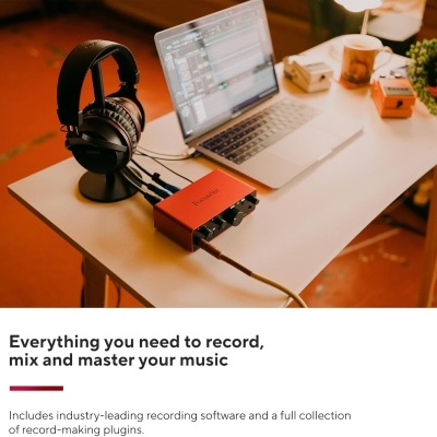 Mesa branca com laptop, auscultadores pretos em suporte e interface de áudio vermelha