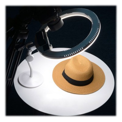 Chapéu de palha castanho claro com fita preta sobre superfície branca iluminada