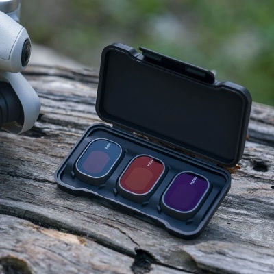 Filtros quadrados coloridos dentro de estojo preto sobre madeira com drone ao lado.