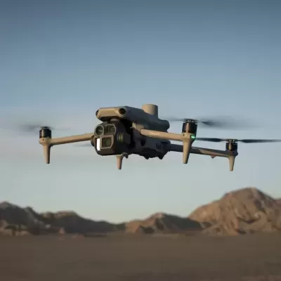 Drone cinza com quatro hélices em voo sobre terra árida com montanhas ao fundo