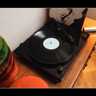 Gira-discos preto com disco vinil sobre mesa de madeira com vaso colorido ao lado