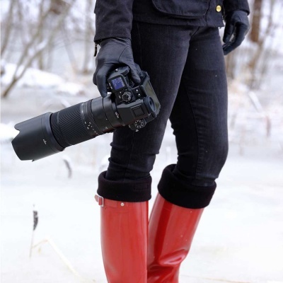 Pessoa com botas vermelhas segurando câmera preta em ambiente nevado
