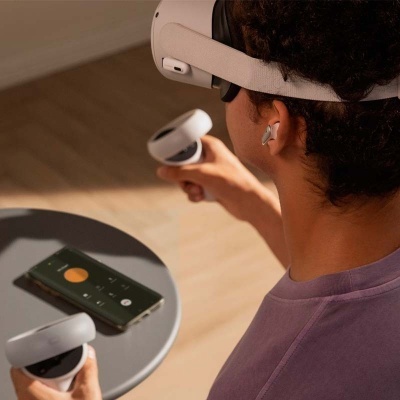 Pessoa com headset de realidade virtual e controladores brancos segurando próximo de mesa com telemóvel