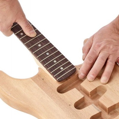 Guitarra elétrica de madeira clara sem acabamento com braço escuro sendo segurada por mãos.