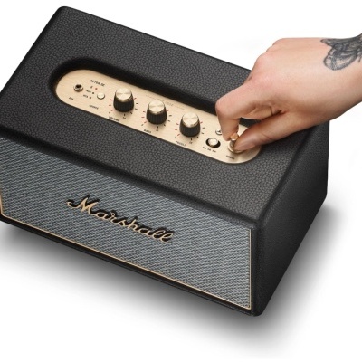 Coluna de som Marshall preta com botões dourados e mão a ligar o power