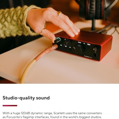 Interface de áudio Focusrite Scarlett 2i2 vermelha com botões pretos e cabo, mão a ajustar, headset ao fundo