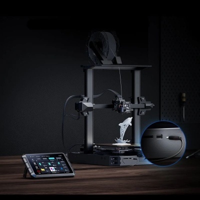 Impressora 3D preta com tablet e figura branca impressa sobre mesa de madeira