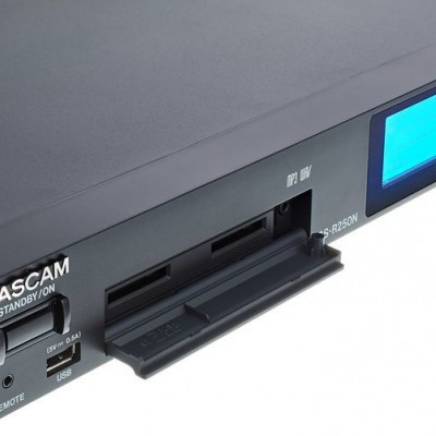 Aparelho de áudio TASCAM preto com visor azul e compartimento aberto