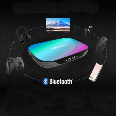 Caixa multimédia HK1 colorida com ecrã digital, rodeada por vários dispositivos eletrónicos e o logo Bluetooth