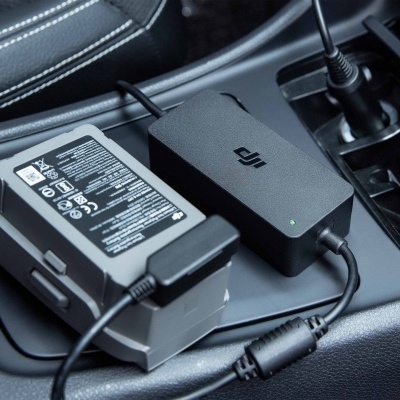 Carregador DJI preto e adaptador cinzento na consola central de um carro