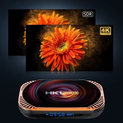 Box de streaming HK1 BOX com visor digital, TVs ao fundo exibindo flor laranja em SDR e 4K ULTRAHD